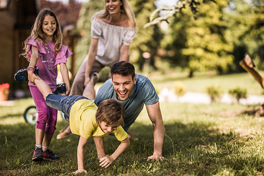 Young cheerful family having fun during wheelbarrow race in the back yard.