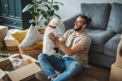 Young men moving in new house. He is happy and playing with his pet dog.