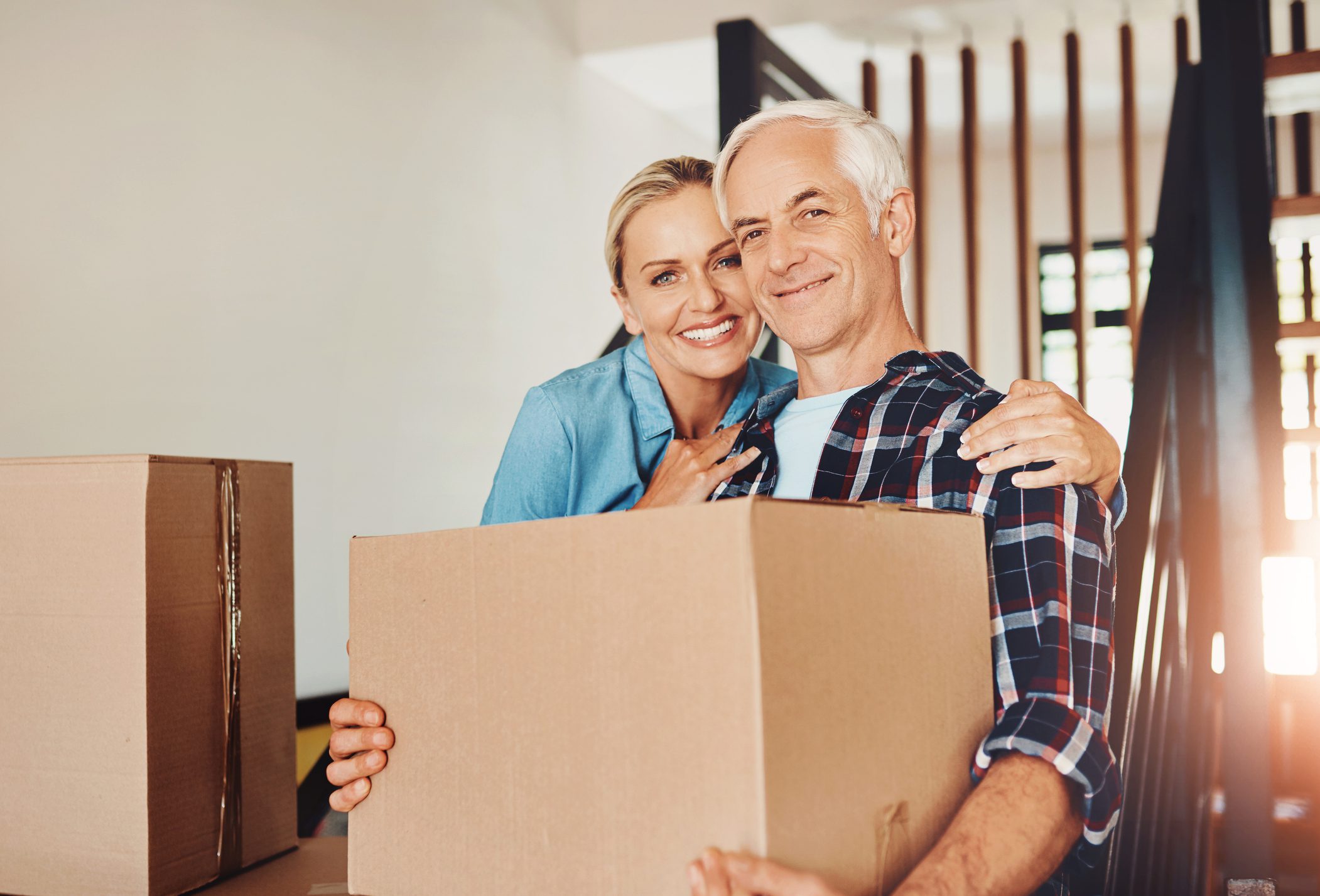 Mature couple, moving and portrait in new home with hug, help and pride for immigration at property. People, woman and man with cardboard container, relocation and investment in real estate